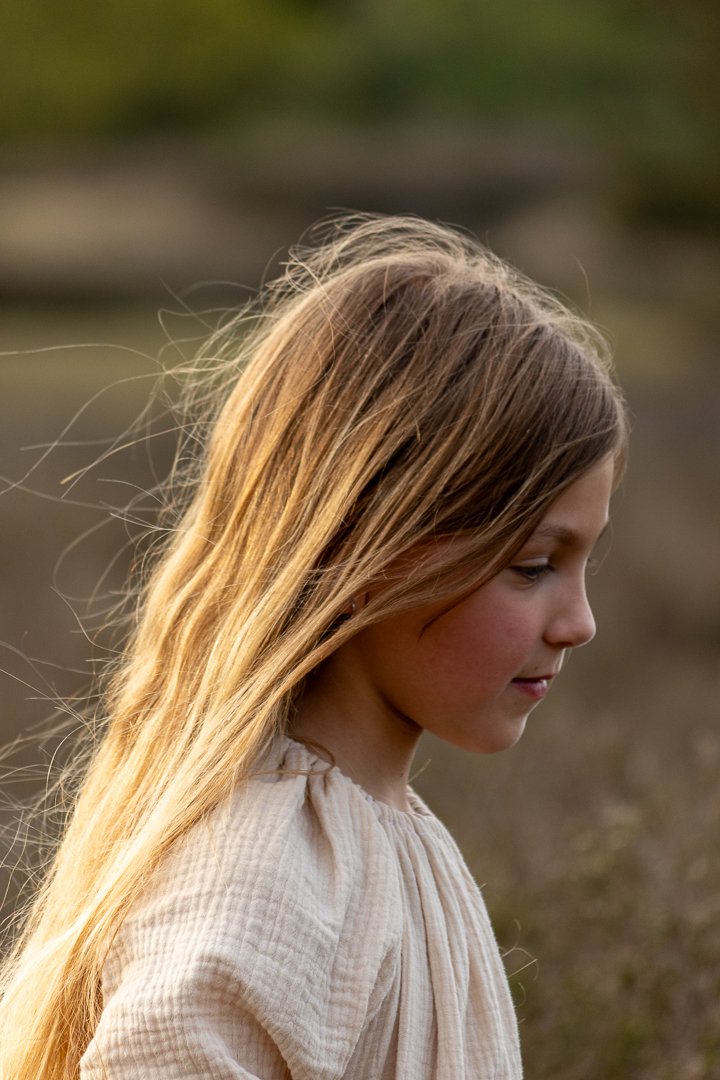 Tienermeisje met lang blond haar die naar beneden kijkt, zonlicht valt mooi op haar haren, familiefotografie.