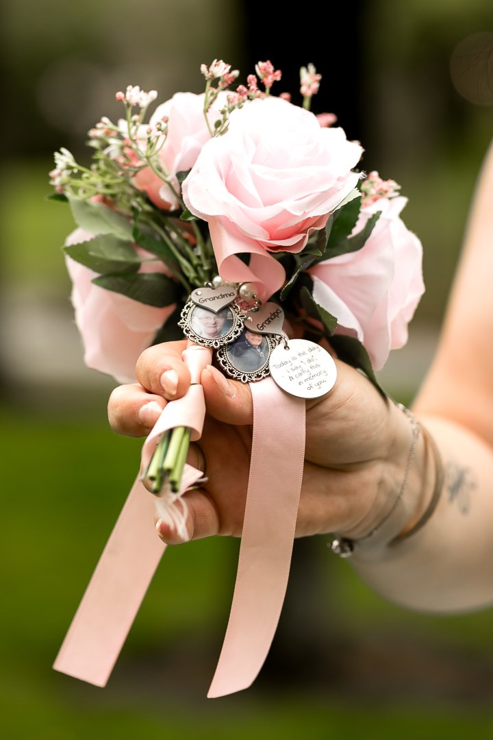 Bruid houdt een bosje roze bloemen met een roze lint en foto- of herinneringsbedels met tekst en foto