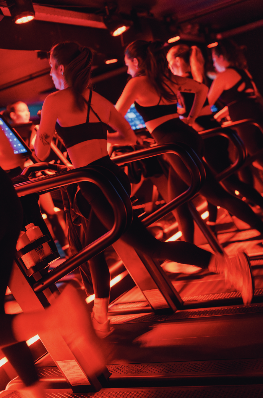 Women exercising on treadmills in a dark, red-lit fitness studio.