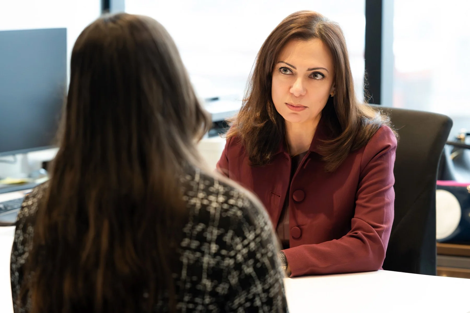 Two women having a serious conversation in an office, with one woman facing the camera and the other with her back to the camera.