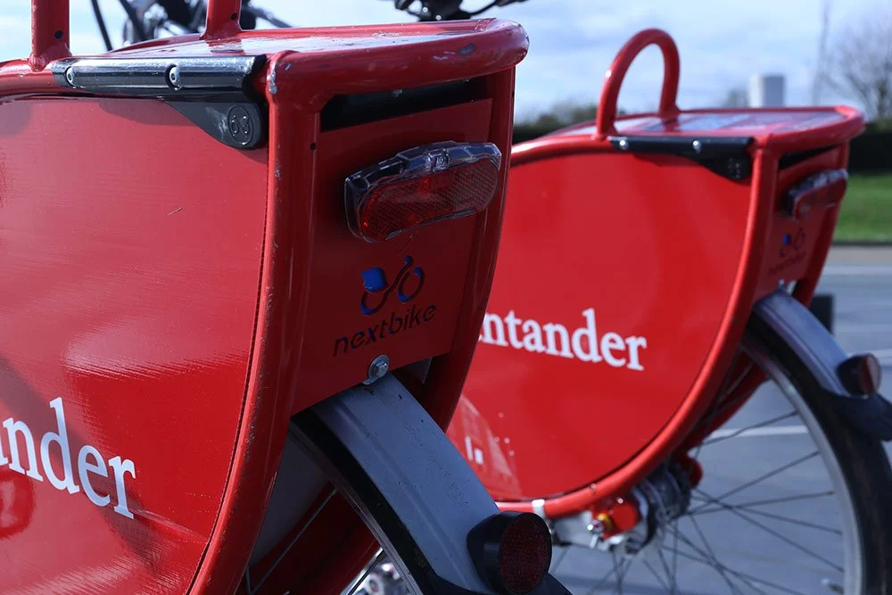 Red Santander bike with rear lights and a small logo for Nextbike, parked outdoors on a bike lane or path.