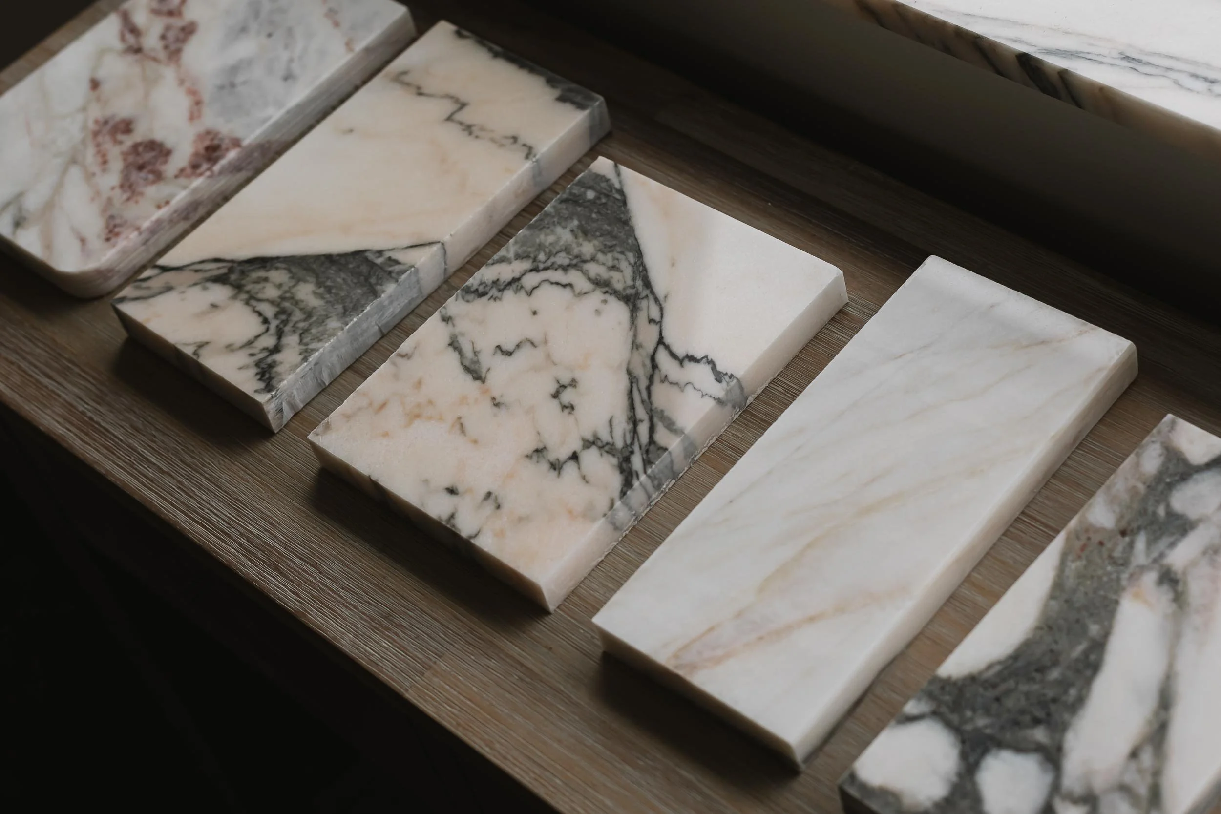 Samples of marble tiles with various patterns and colors displayed on a wooden surface.