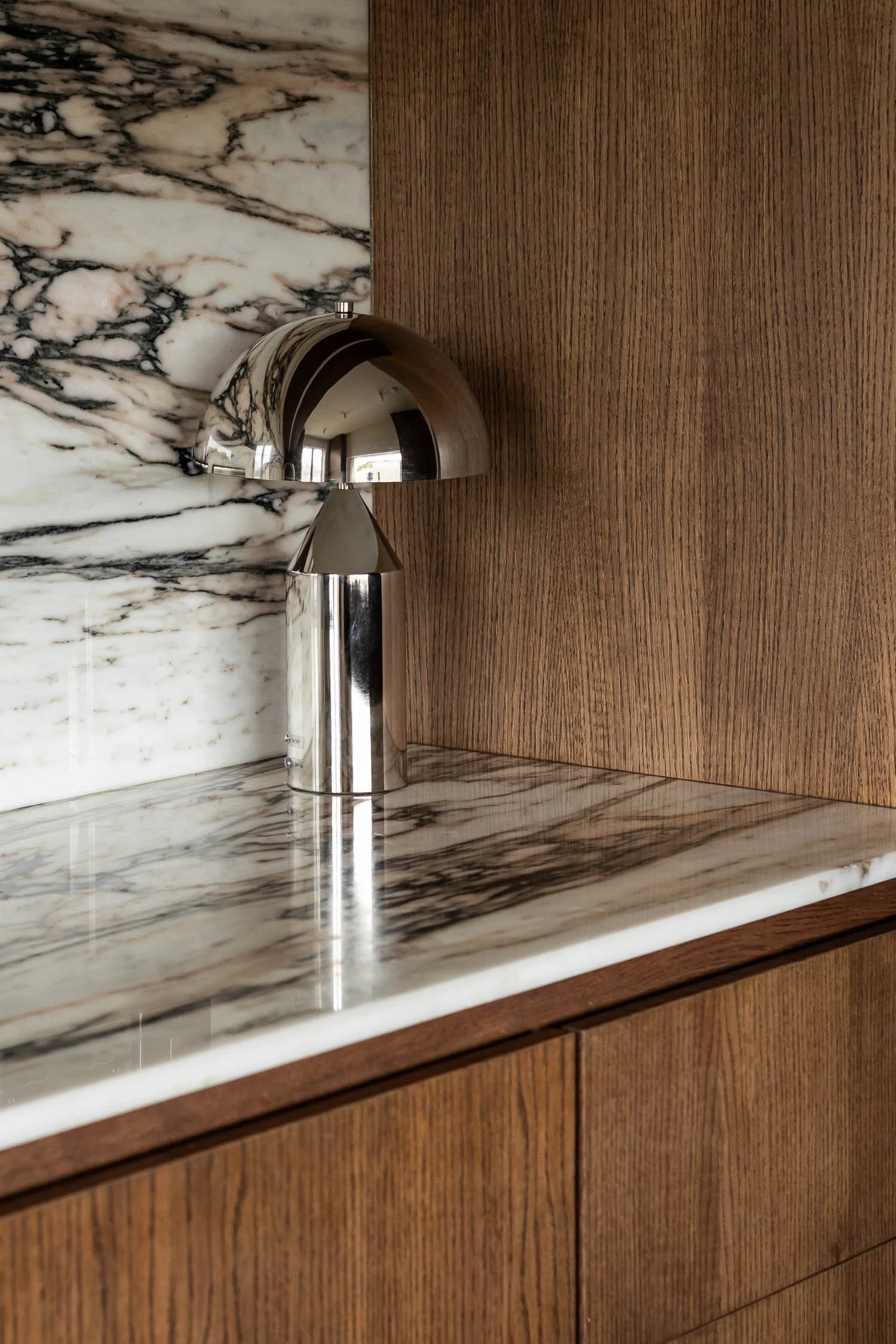Close-up of a modern kitchen sink with a stainless steel faucet, marble countertop and backsplash, and wooden cabinets.
