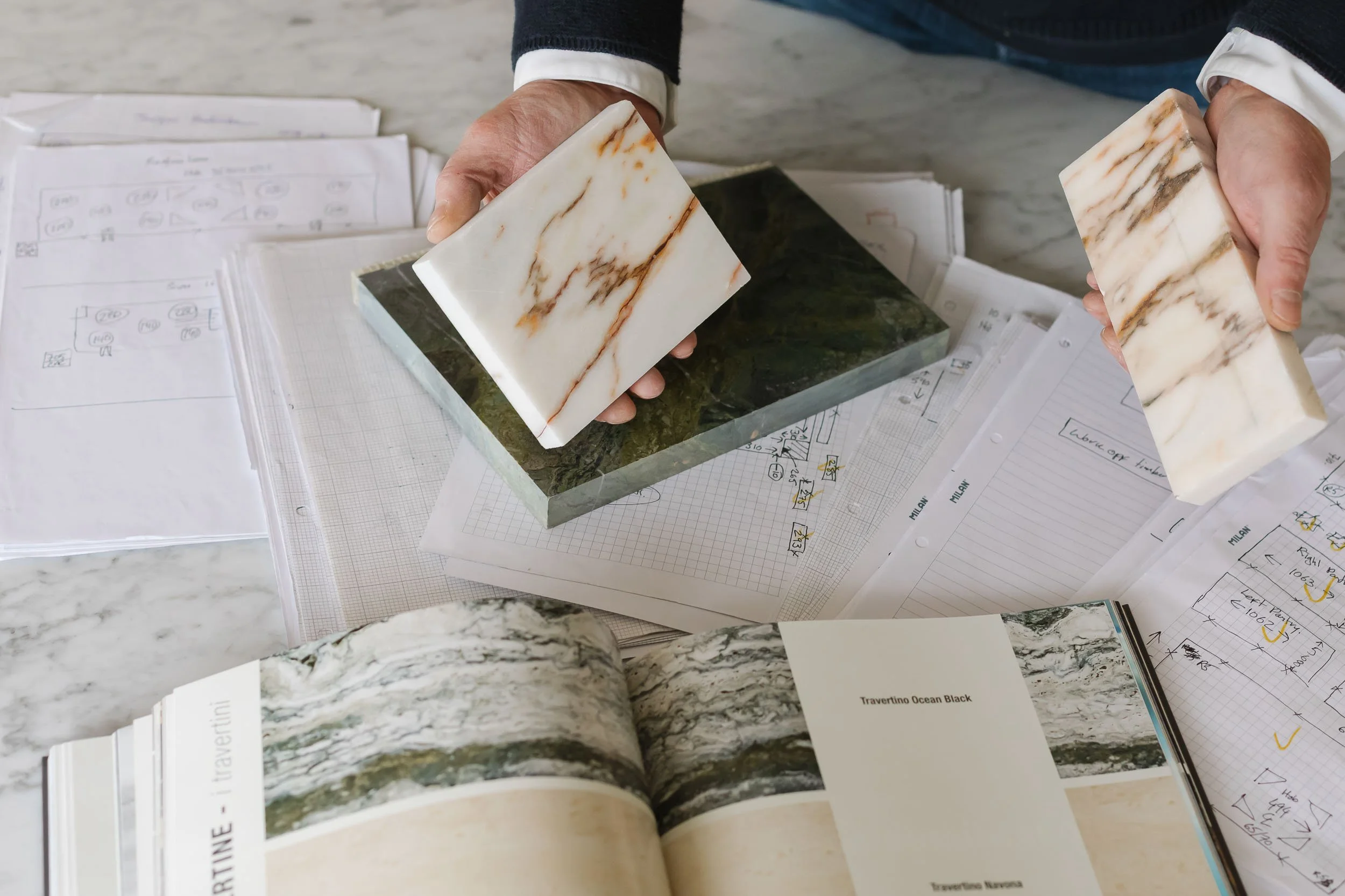 Hands holding marble tiles above papers and documents on a marble surface.