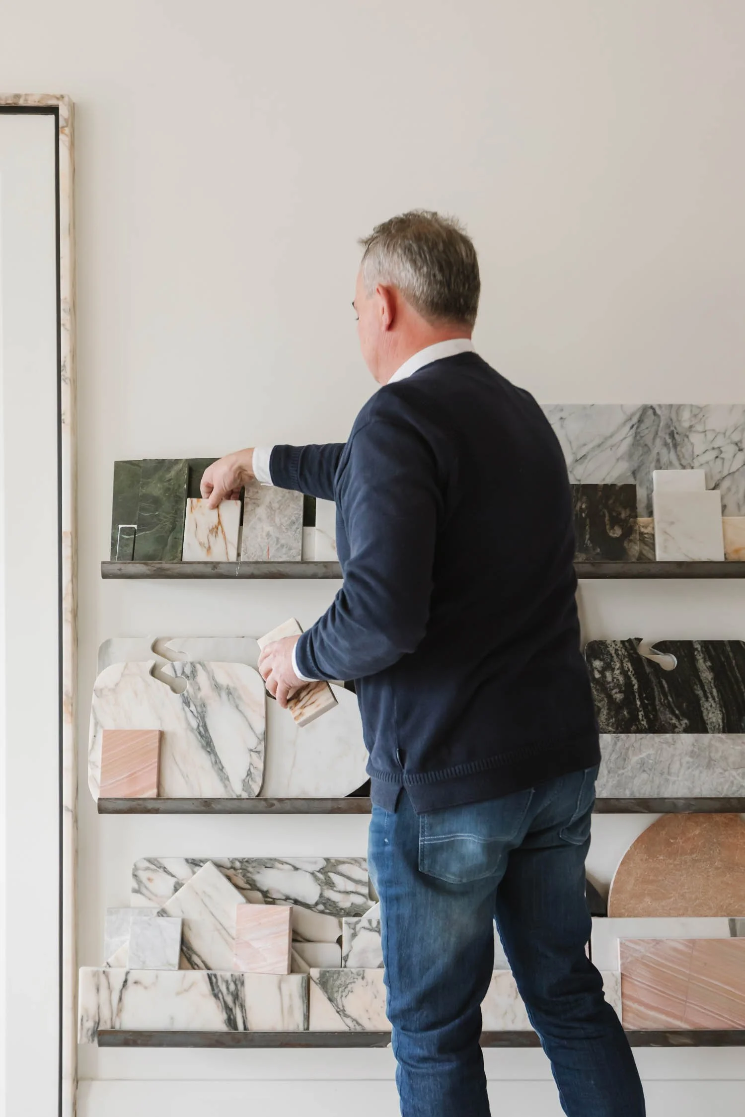 A man in a dark jacket and jeans shopping for marble samples in a store.