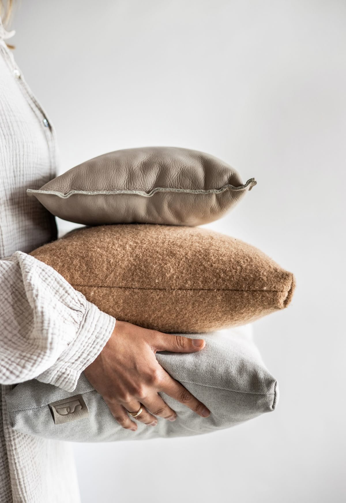 Person holding three pillows stacked on top of each other against a plain background.