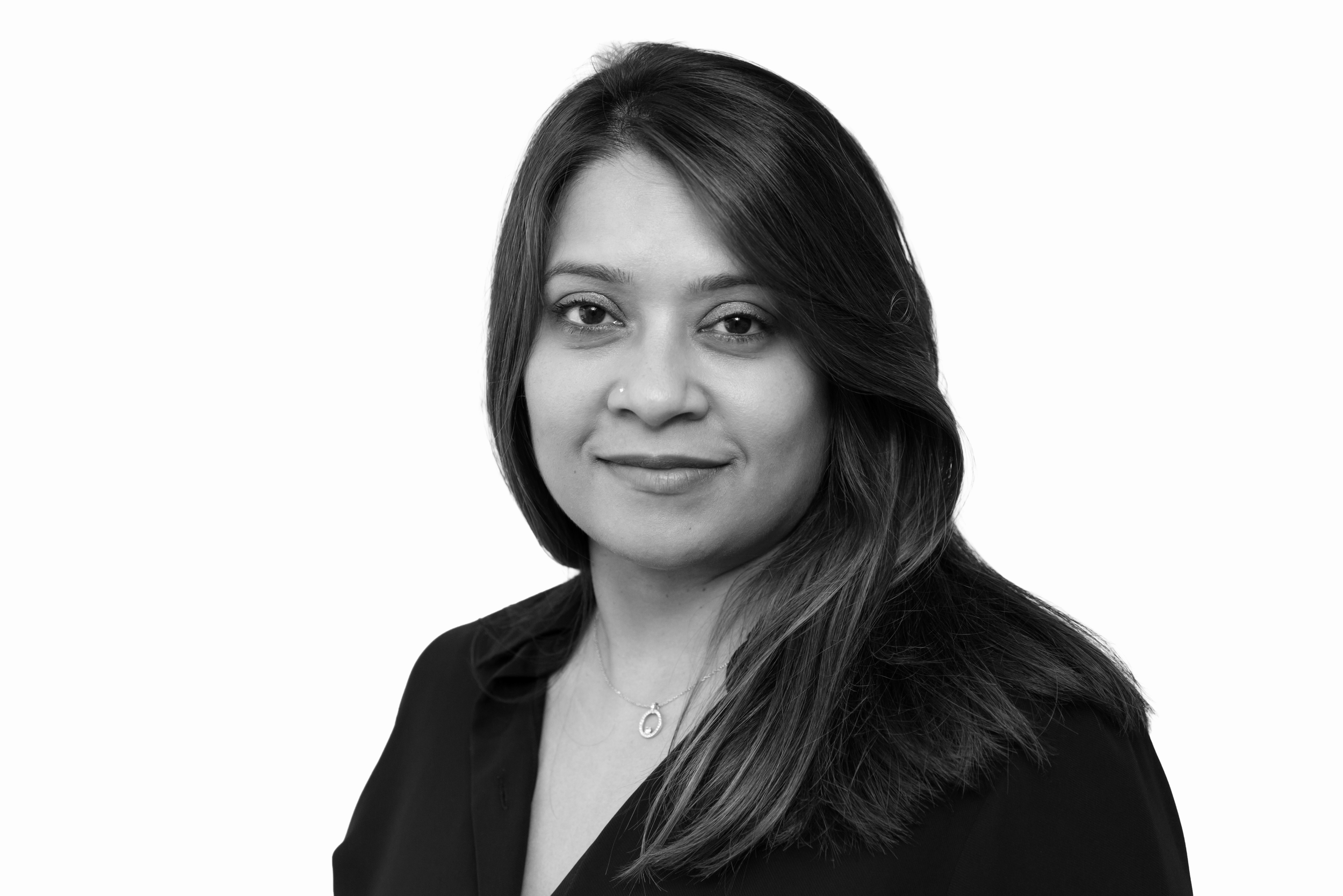 A black-and-white headshot of a woman with long hair, wearing a dark blazer and a necklace, looking at the camera with a slight smile.
