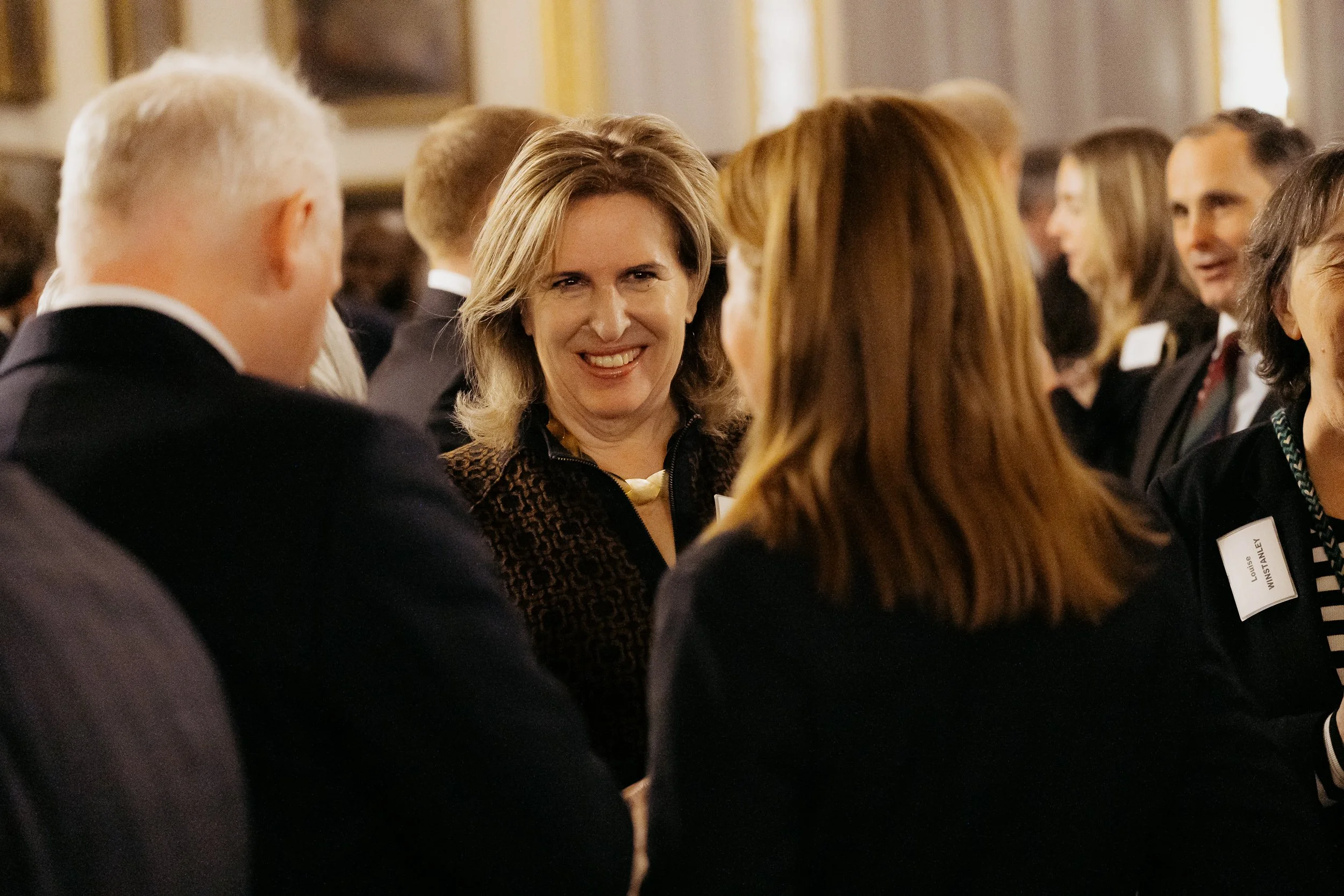A group of people dressed in formal attire engaged in conversation at an indoor event.