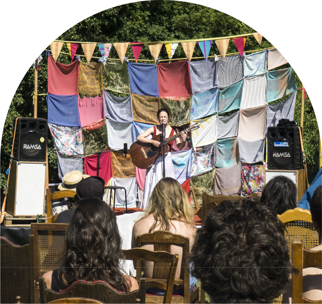 A musician performing on an outdoor stage in front of a seated audience.