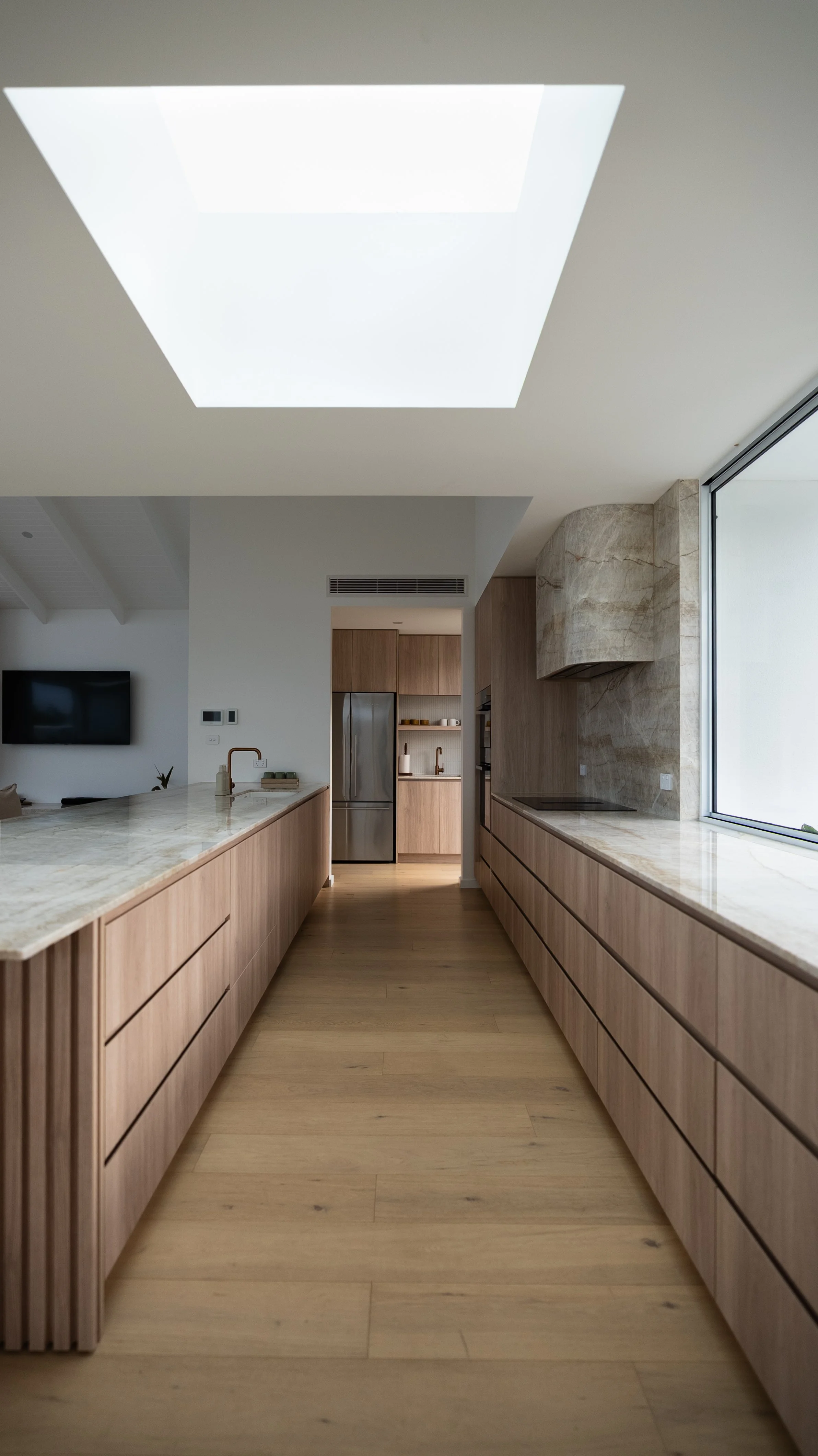 Modern kitchen with light wood cabinets, marble countertops, a skylight, and a large window.