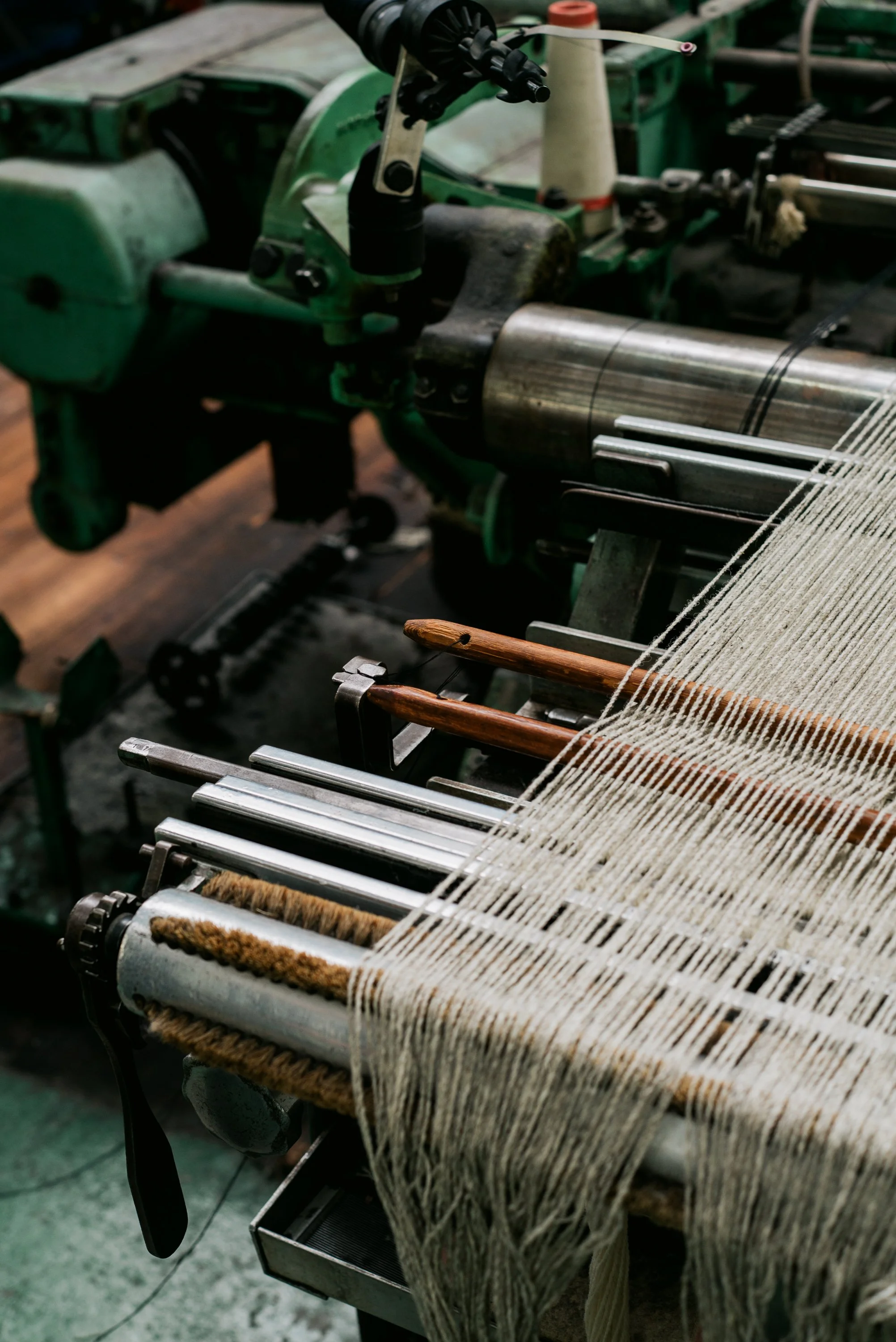A textile loom machine with white yarn, metal parts, and wooden tools involved in the weaving process.