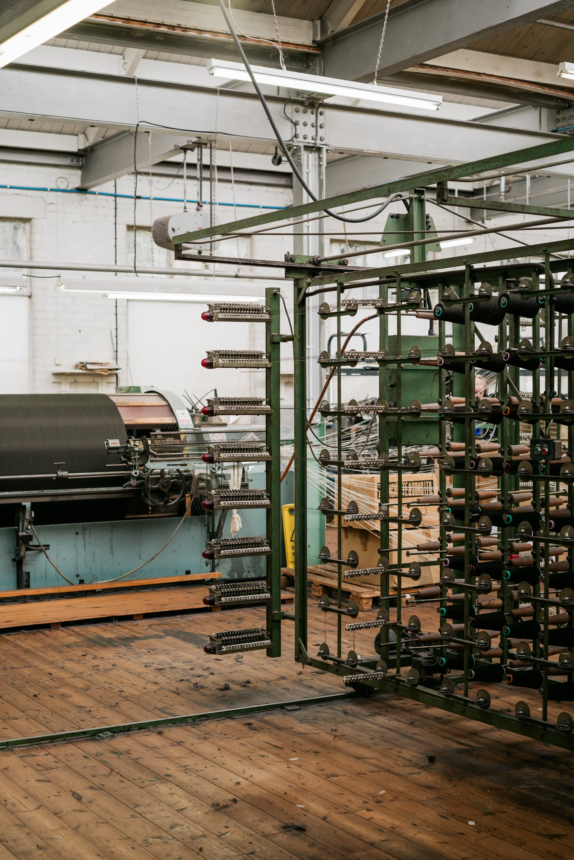 Industrial textile manufacturing setup with rolling machines, spools of thread, and a wooden floor.