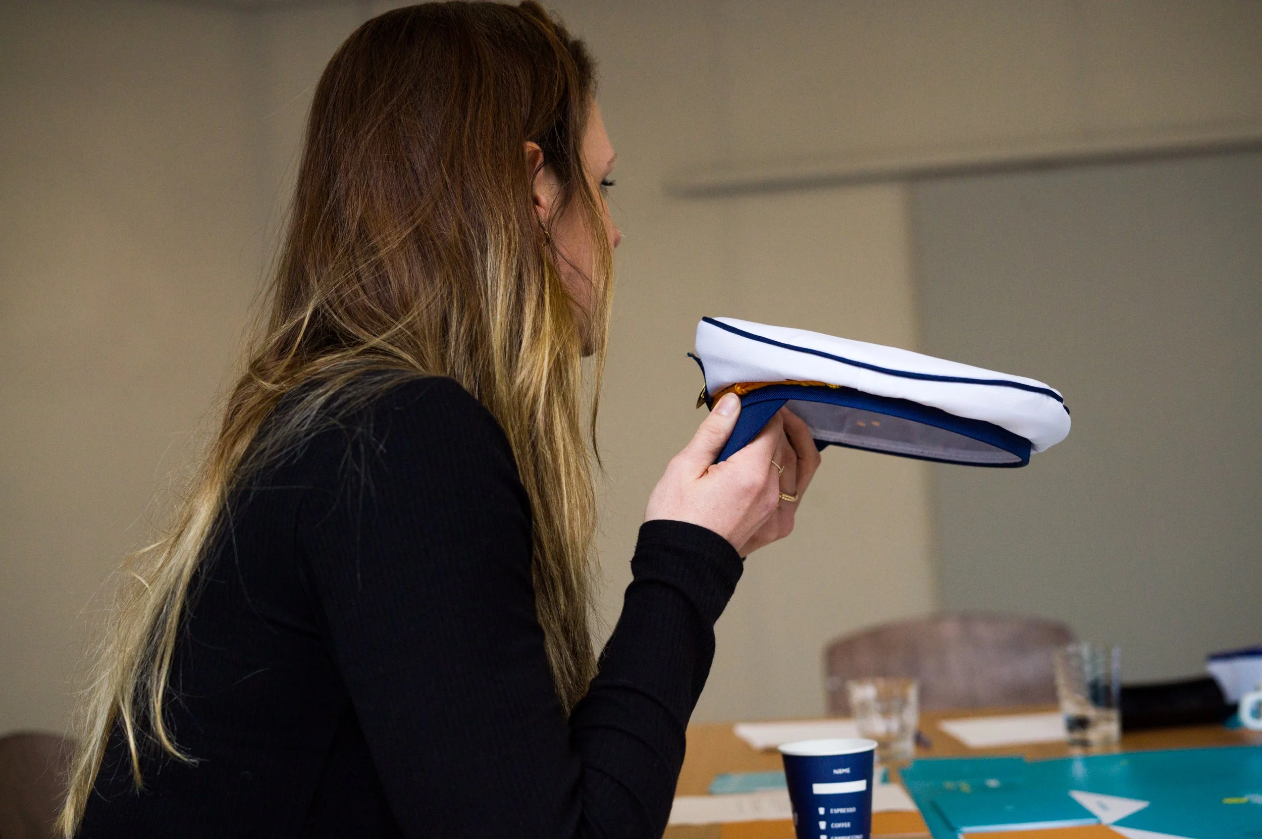 Vrouw met lang haar die een witte en blauwe pet vasthoudt tijdens een bijeenkomst waarin het Boordspel gespeeld wordt.