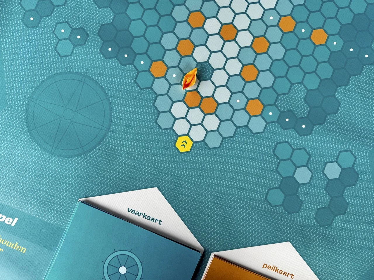 Een speelbord met een hexagonale indeling, enkele blauwe en oranje speelkaarten met tekst.