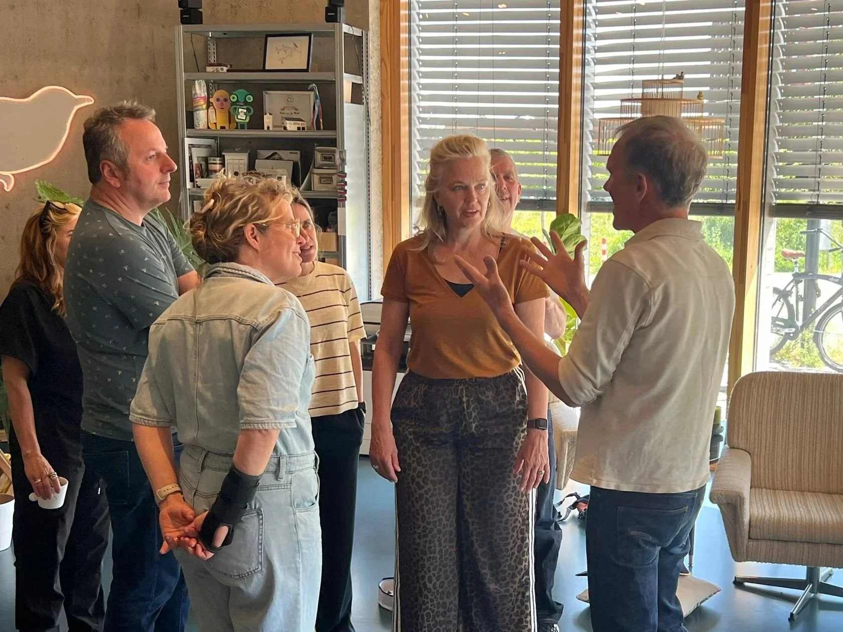 Een groep mensen die in een gesprek verwikkeld is binnen een interieur met grote ramen. Ze zijn bezig met het Boordspel.