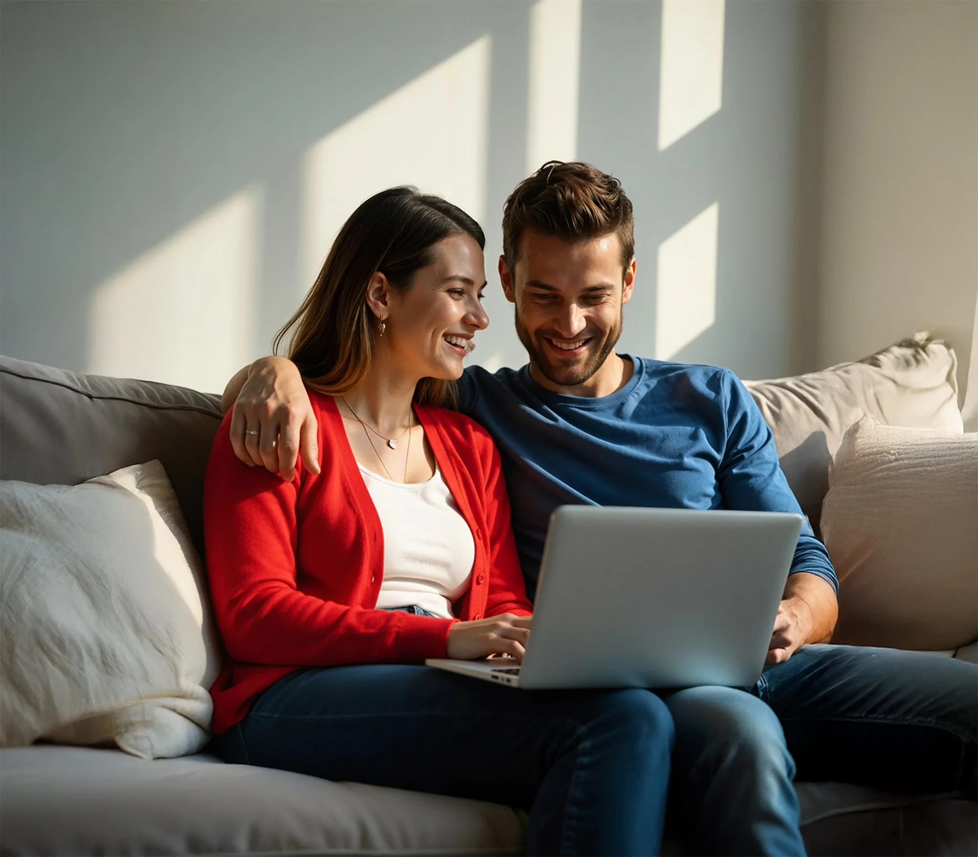 Um casal sorridente sentado no sofá, assistindo algo em um laptop.