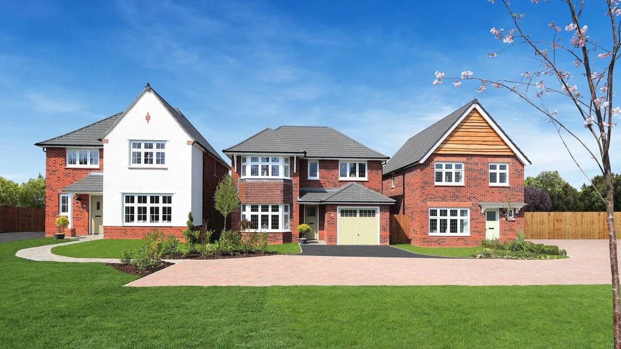 Three modern brick houses with well-maintained lawns, a paved driveway, and a clear blue sky in a suburban neighborhood.