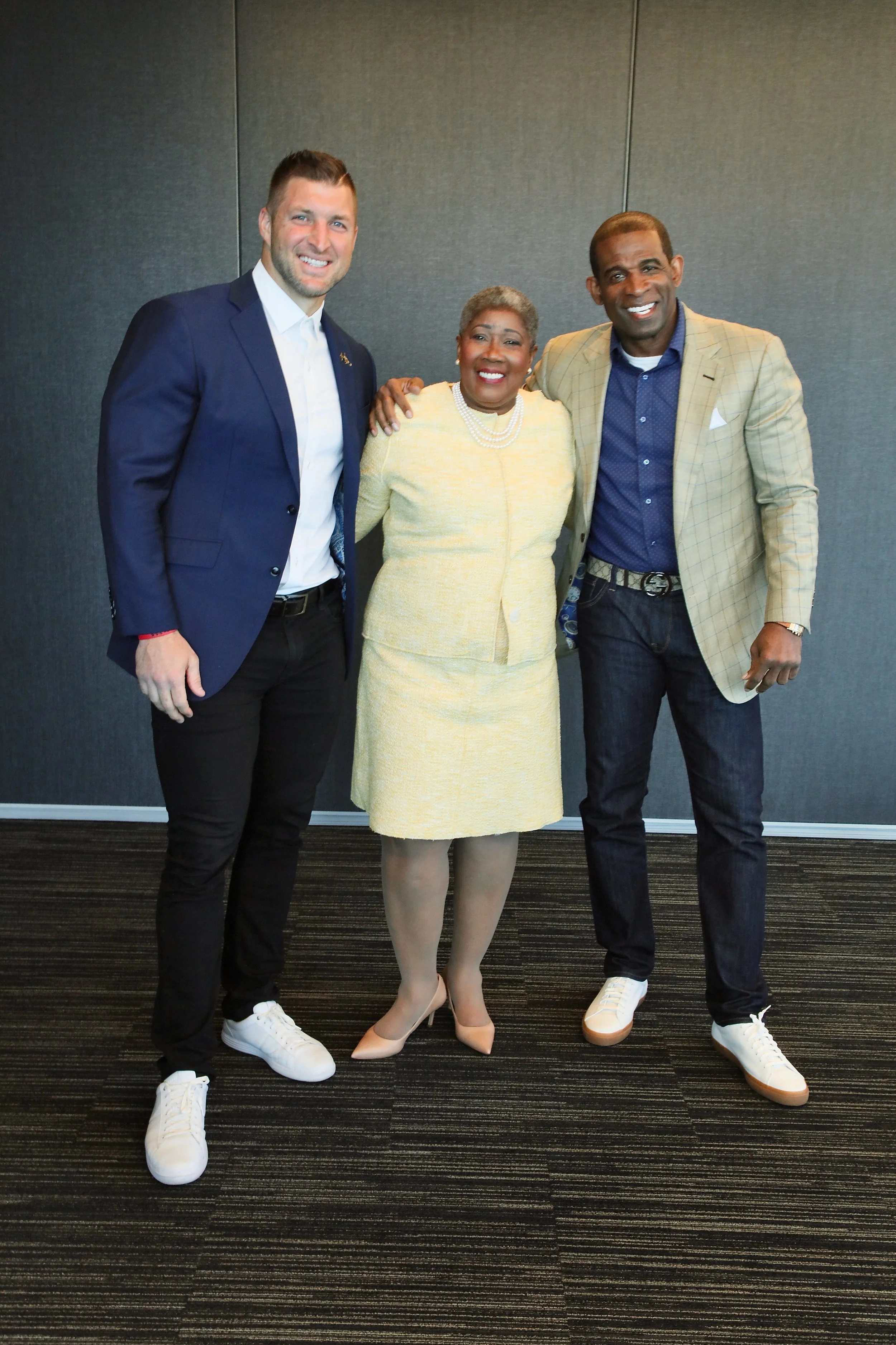 Three people standing together indoors, smiling for the camera. They are dressed in business casual attire.