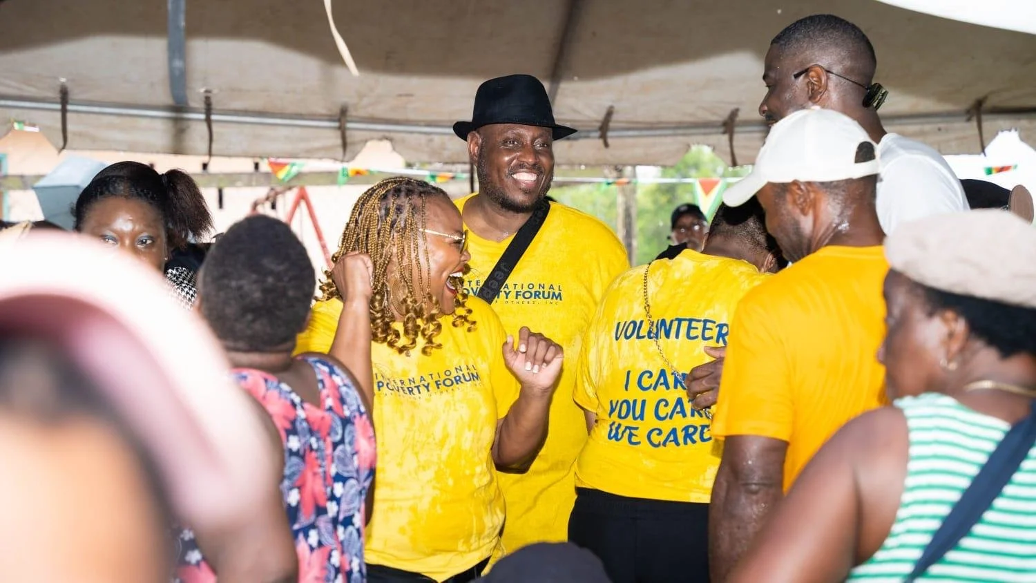 Group of people wearing yellow volunteer T-shirts inside a tent, smiling and interacting enthusiastically.