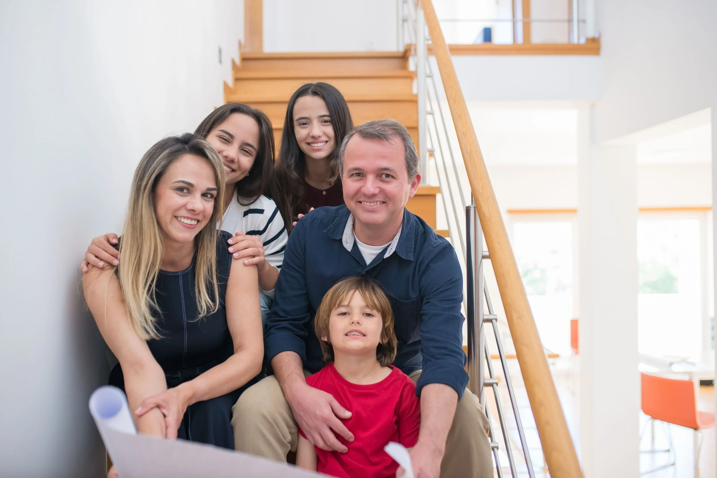 A family of five sitting on a staircase inside a bright, modern home, smiling and looking at the camera.