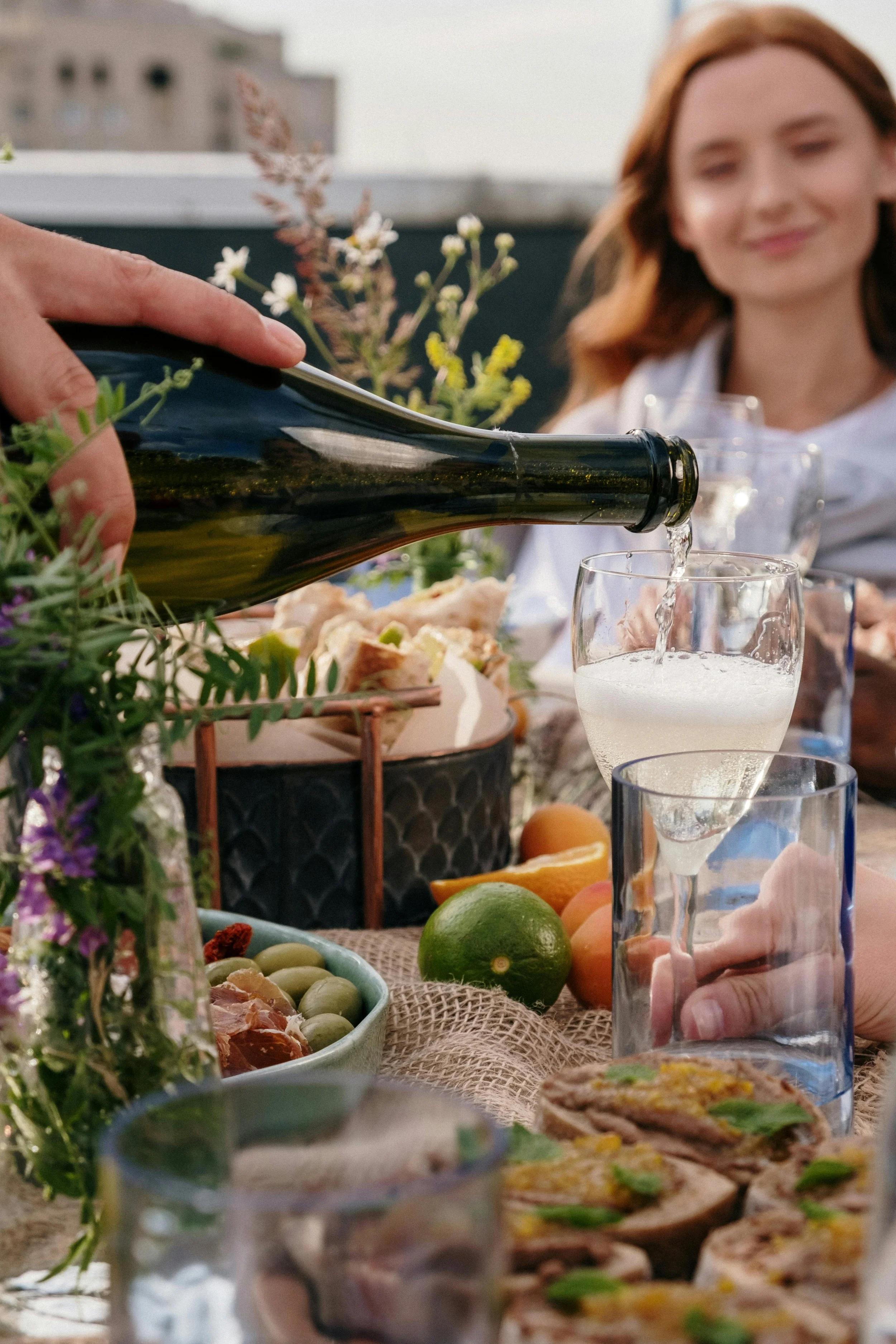 People enjoying a meal outdoors with wine, fruits, and appetizers on a table.