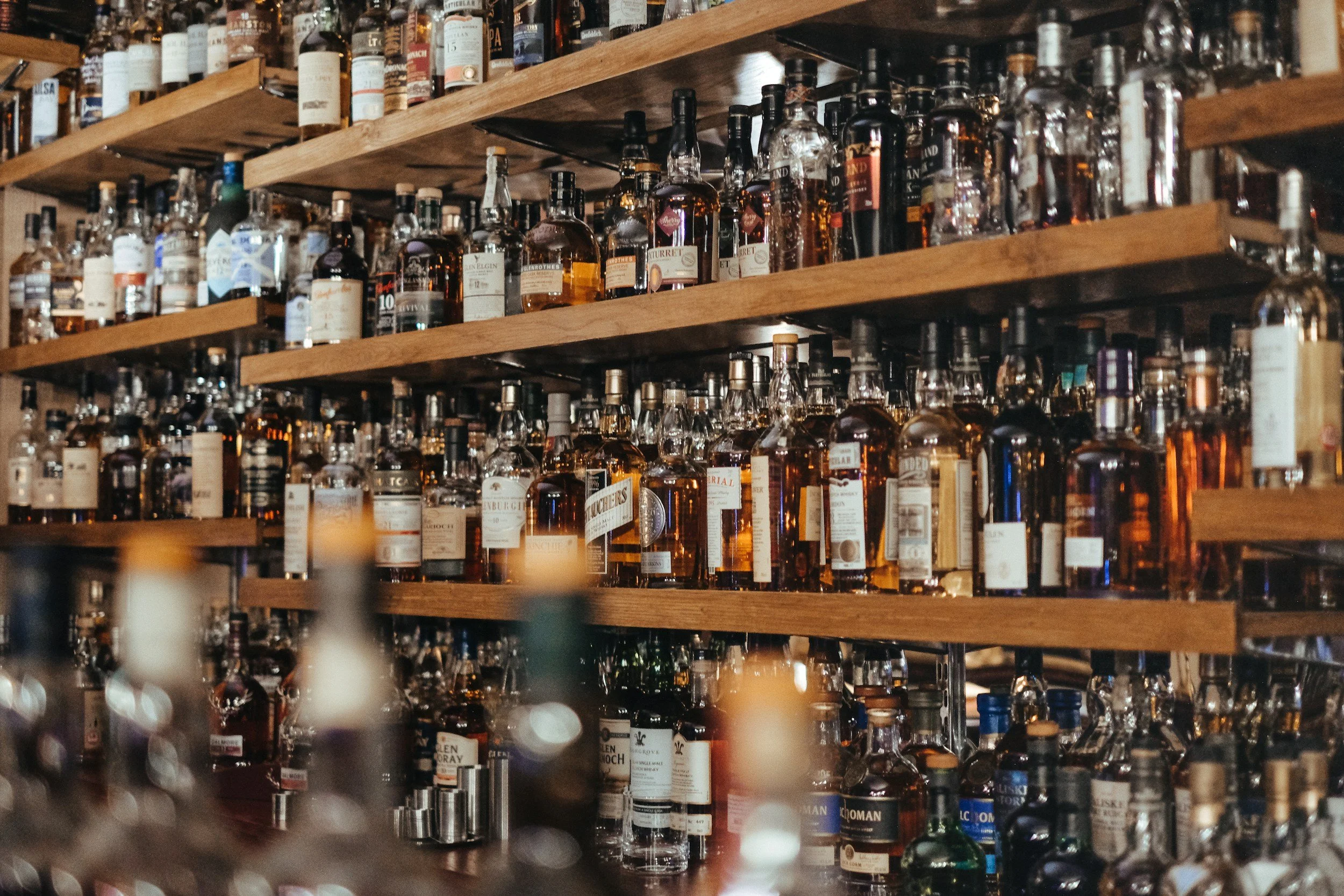 Multiple shelves filled with various bottles of liquor, mostly whiskey, on wooden shelves in a bar or liquor store.
