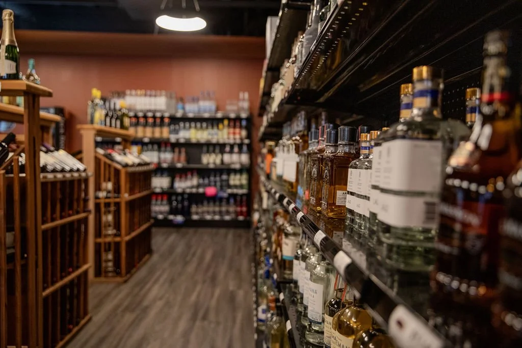 Liquor bottles on shelves and wine on wooden racks in a liquor store aisle.