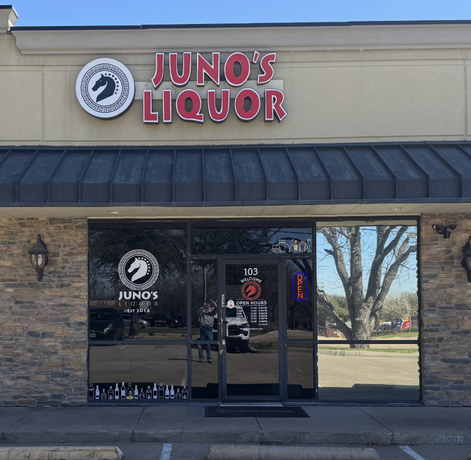 Front view of Juno's Liquor store with signage, glass door, and large windows, reflecting trees and cars outside.