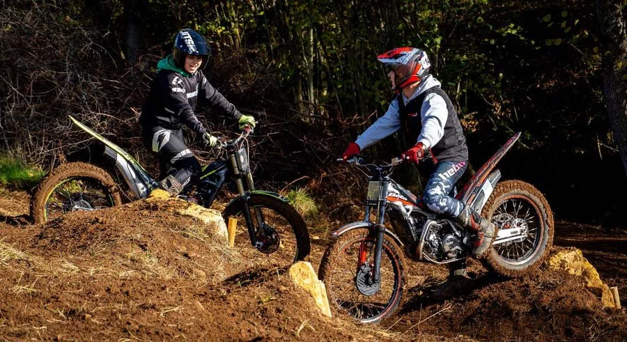 Two riders attempting a rocky technical section together, working on controlled climbs.