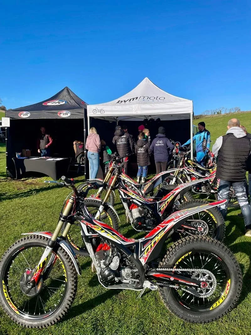 Multiple trials bikes displayed beside event tents at Magnum Trials Centre.