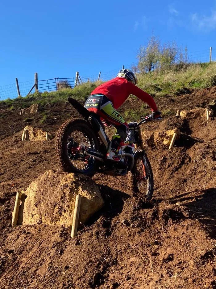 A rider climbing a rocky, sunlit practice section with a strong wheel lift.