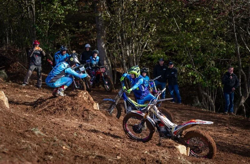 Two riders tackling a steep, muddy bank during a group trials session.