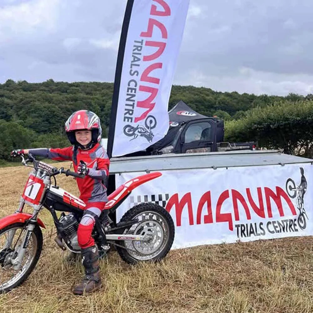Young trials rider with Magnum Trials Centre banner at the Winchcombe training area.