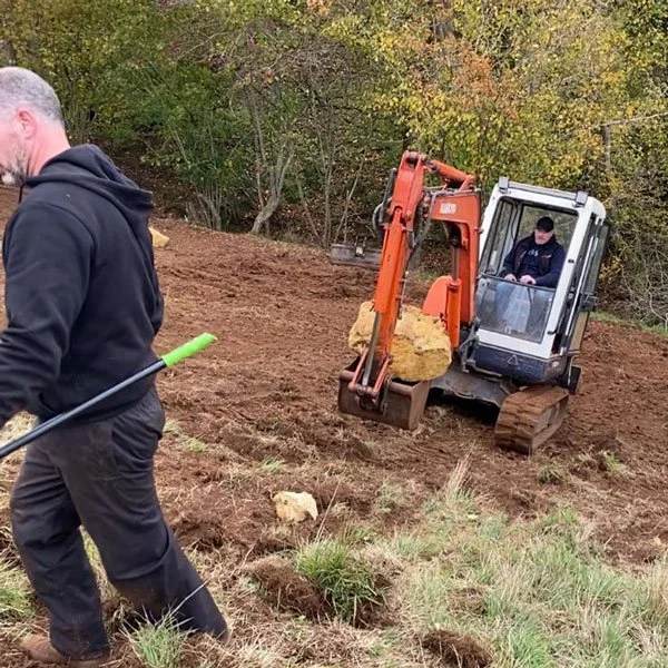 A worker and a mini digger moving large rocks while shaping new off road trials sections at Magnum Trials Centre.