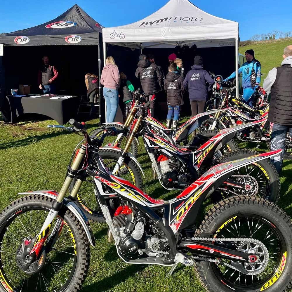 Line of trials bikes and riders at Magnum Trials Centre event village in Winchcombe.
