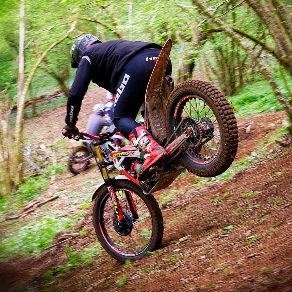 Motorcycle trials rider performing a controlled wheelie on woodland terrain at Magnum Trials Centre.