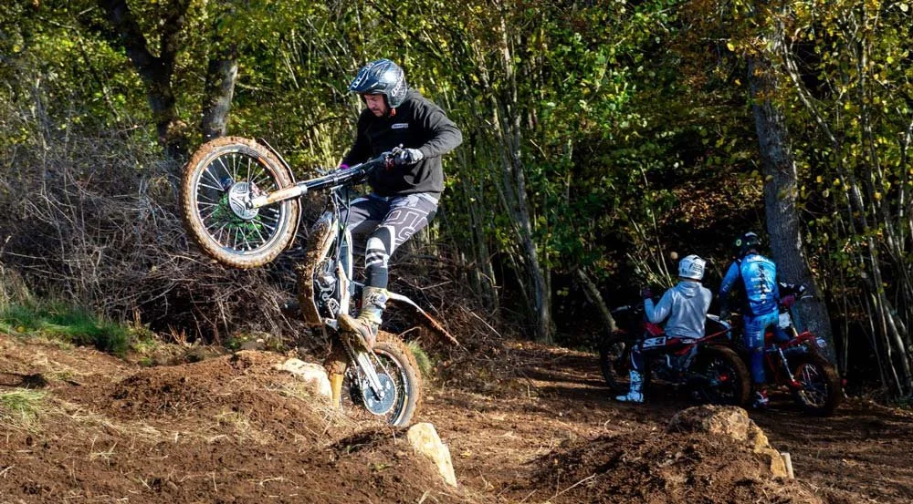 A rider lifting the front wheel while navigating a woodland slope during trials practice.
