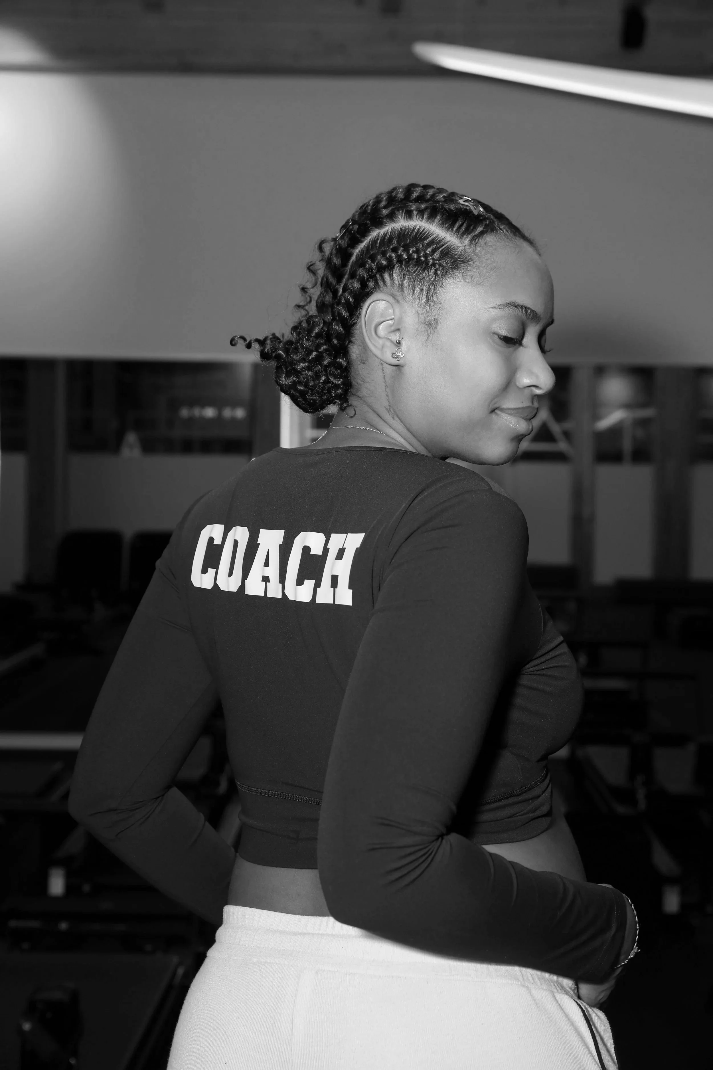 Une femme portant un t-shirt avec le mot 'COACH' inscrit dans le dos, dans un environnement intérieur.