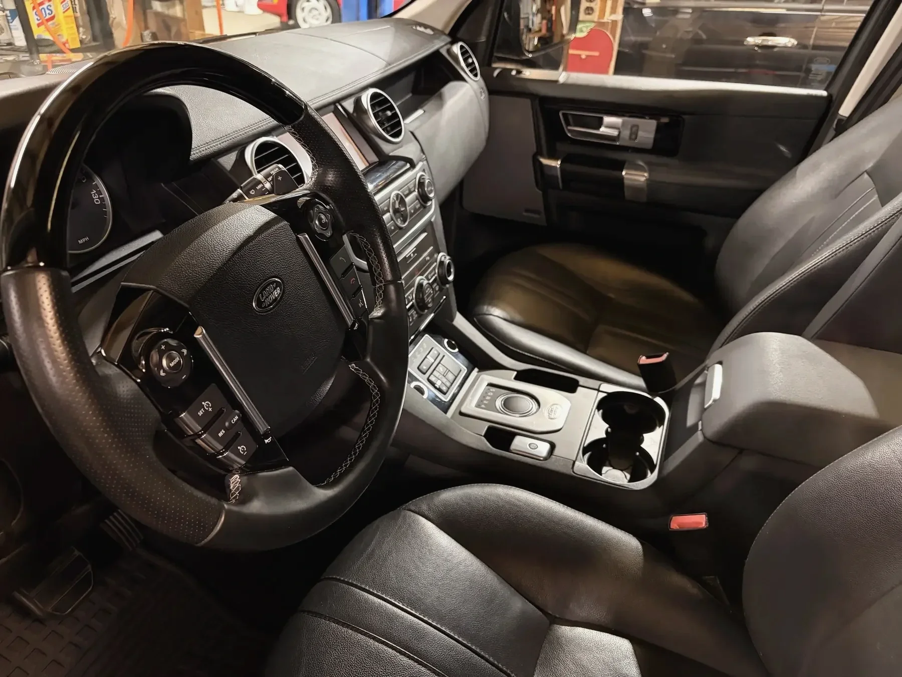 Interior of a Land Rover vehicle showing the dashboard, steering wheel, front seats, and center console with controls and a cup holder.