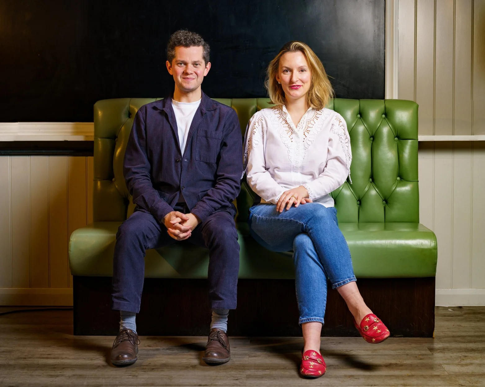 James Way and Natalie Burch sitting on a green cushioned bench in a cosy, well-lit room.