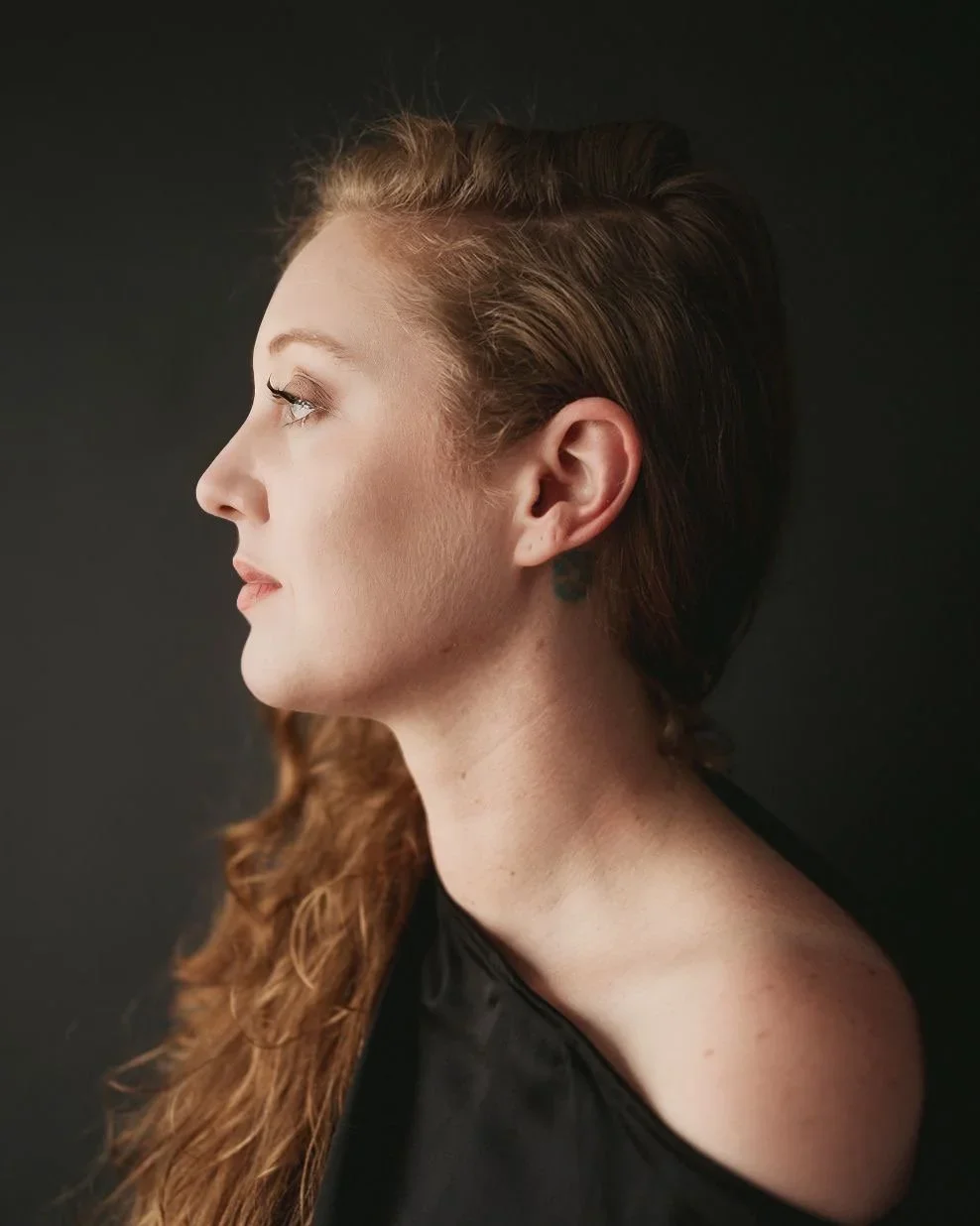 Side profile of  Claire Lees, a woman with red hair against a dark background.