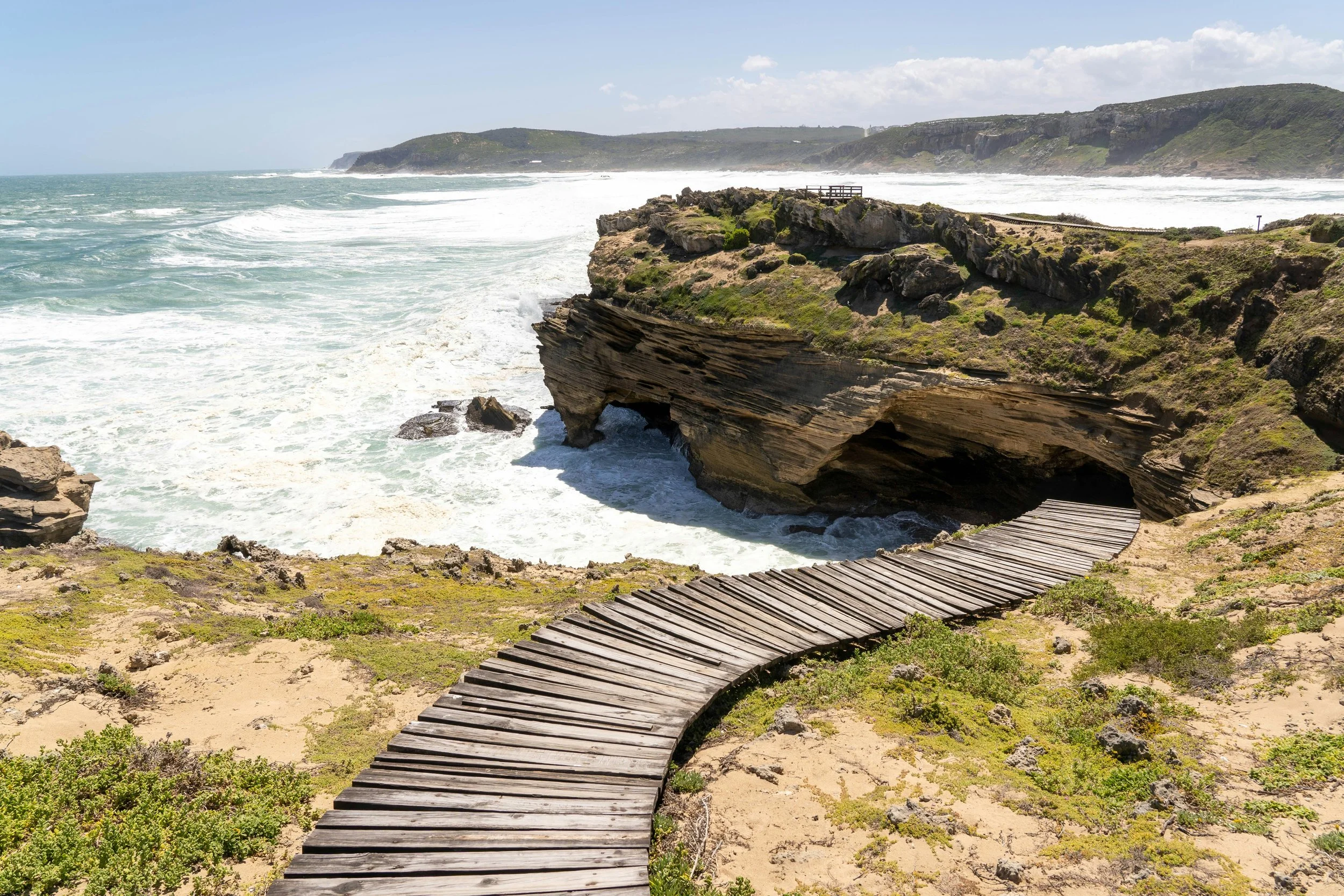 Wooden coastal walkway on Robberg Peninsula leading to rocky cliffs overlooking the Indian Ocean.