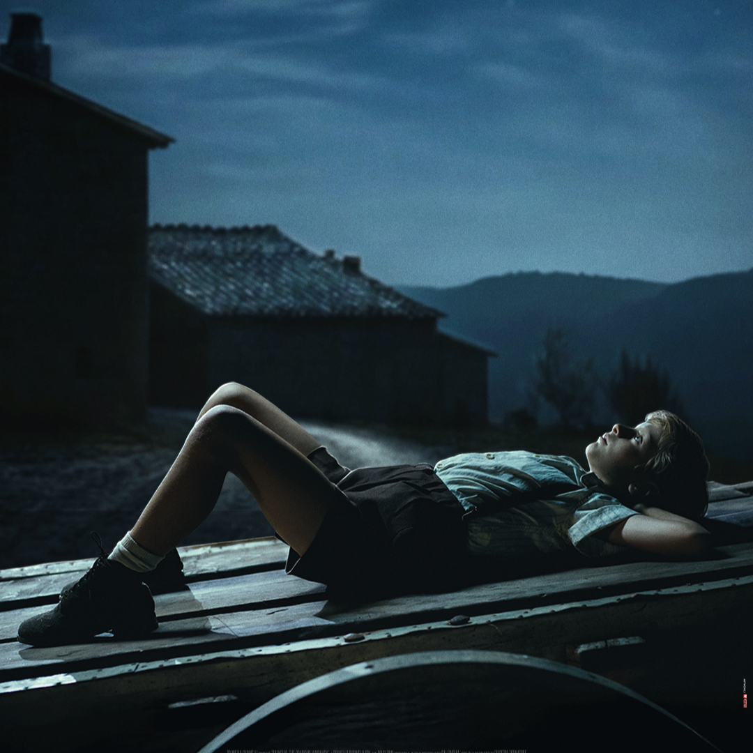 A man standing in a room filled with tall stacks of books on shelves and tables.
