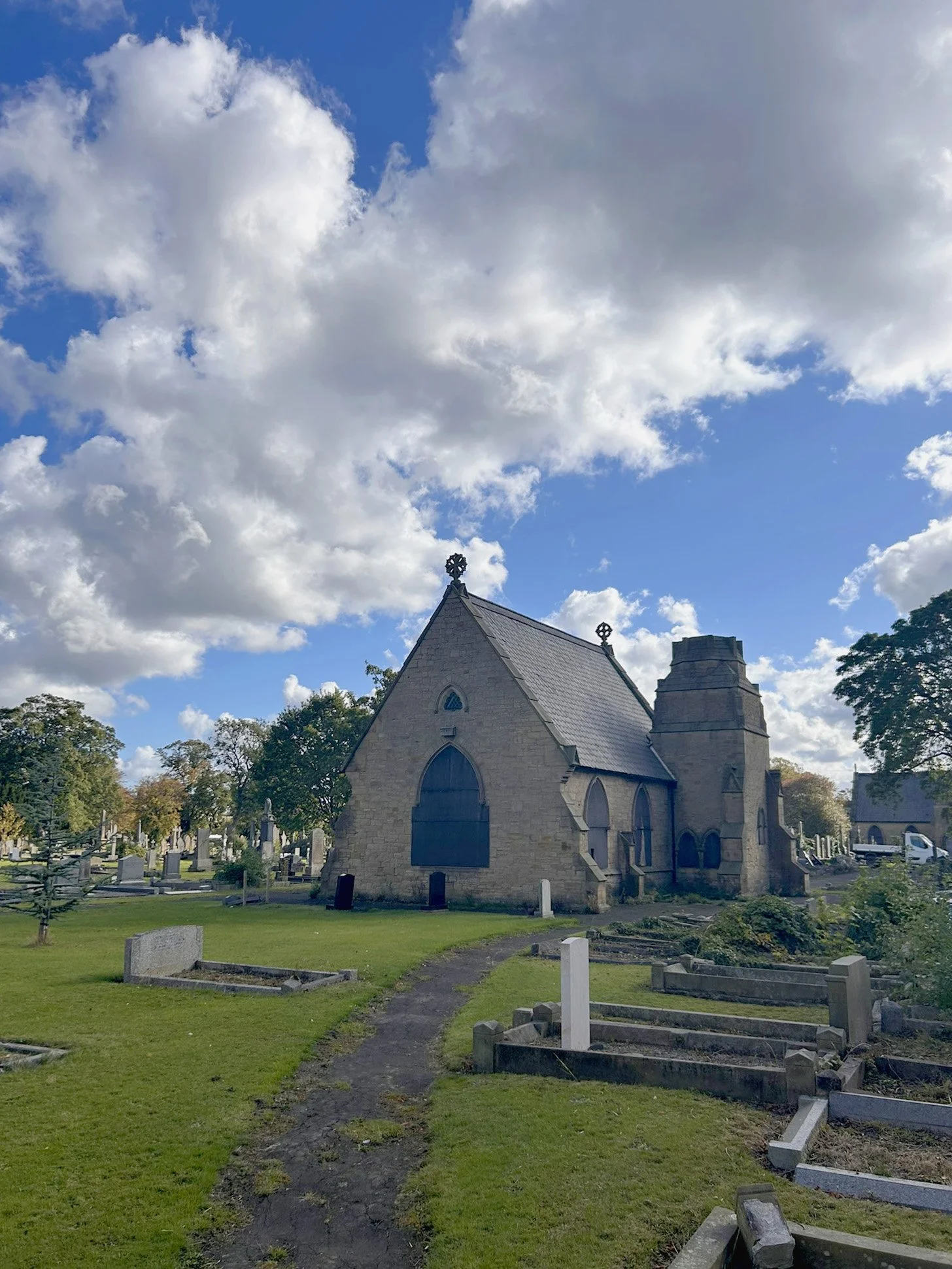 Stone church with gothic architectural elements and a graveyard in the foreground, under a partly cloudy sky.