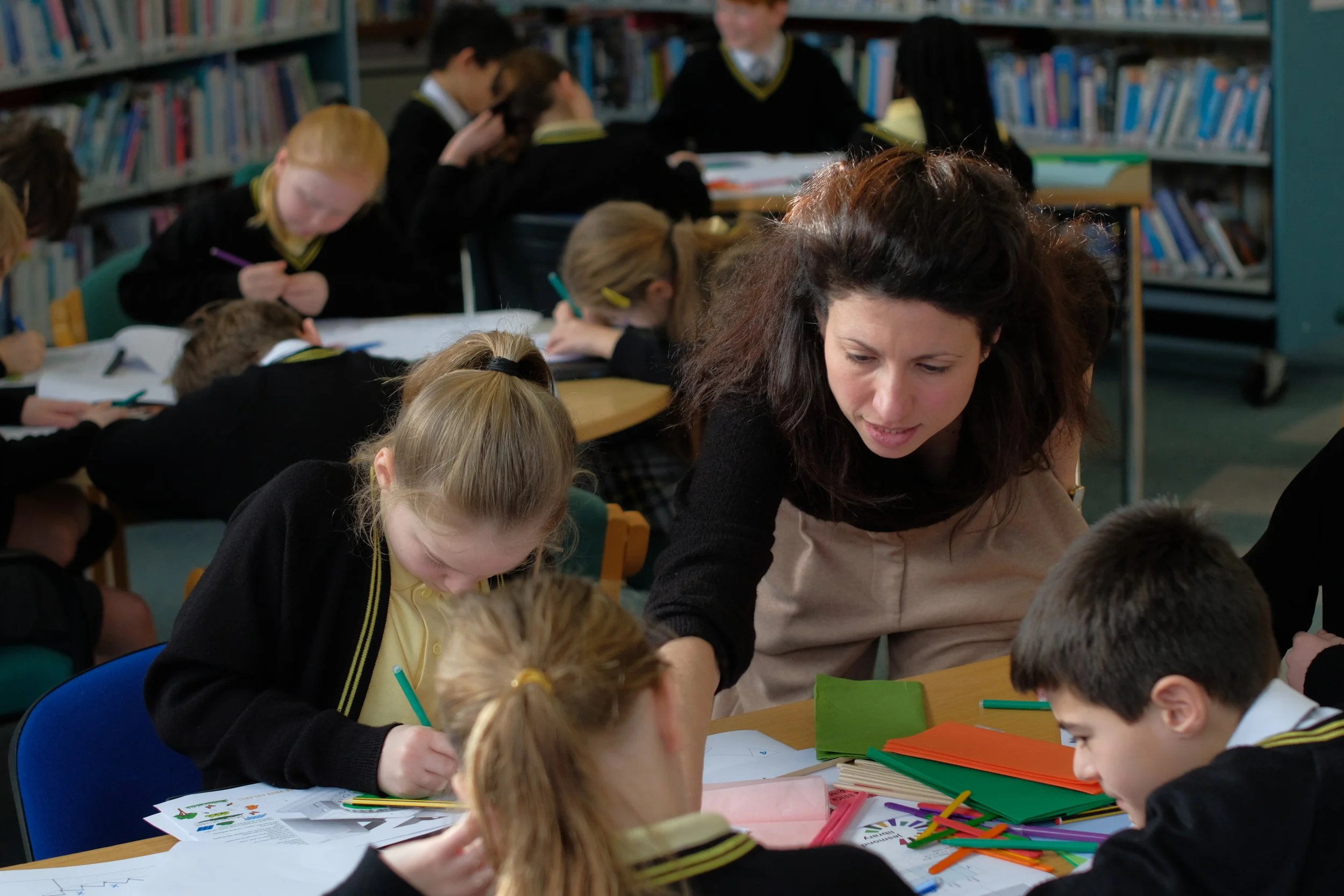 Elementary school classroom with students and teacher working on classroom activities at a table, with school books and supplies around.