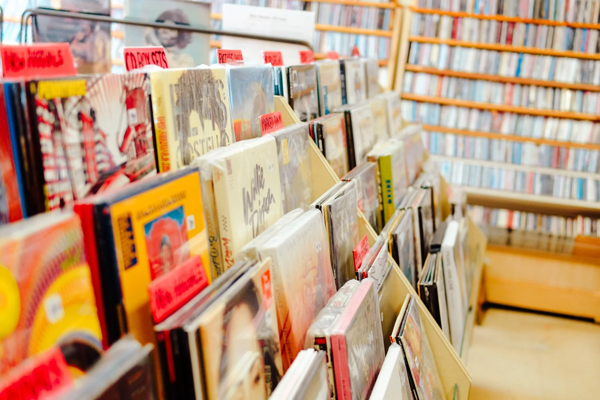 Record shelves filled with various collectible records, with a perspective showing shelves of colourful CDs in the background