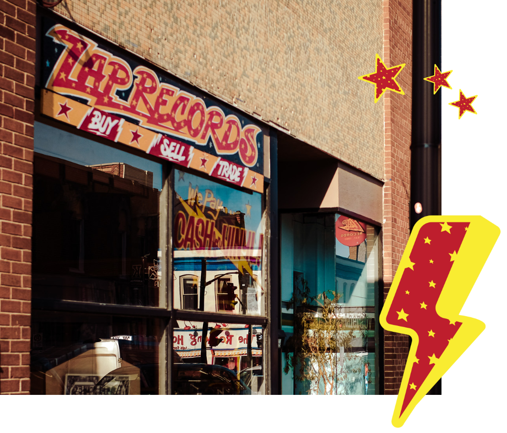 View of a storefront with a sign that reads '7H Records' and encourages buying, selling, and trading records. Reflective glass windows display the street and nearby buildings, with a brick exterior and some decorative stars and a lightning bolt overlay.