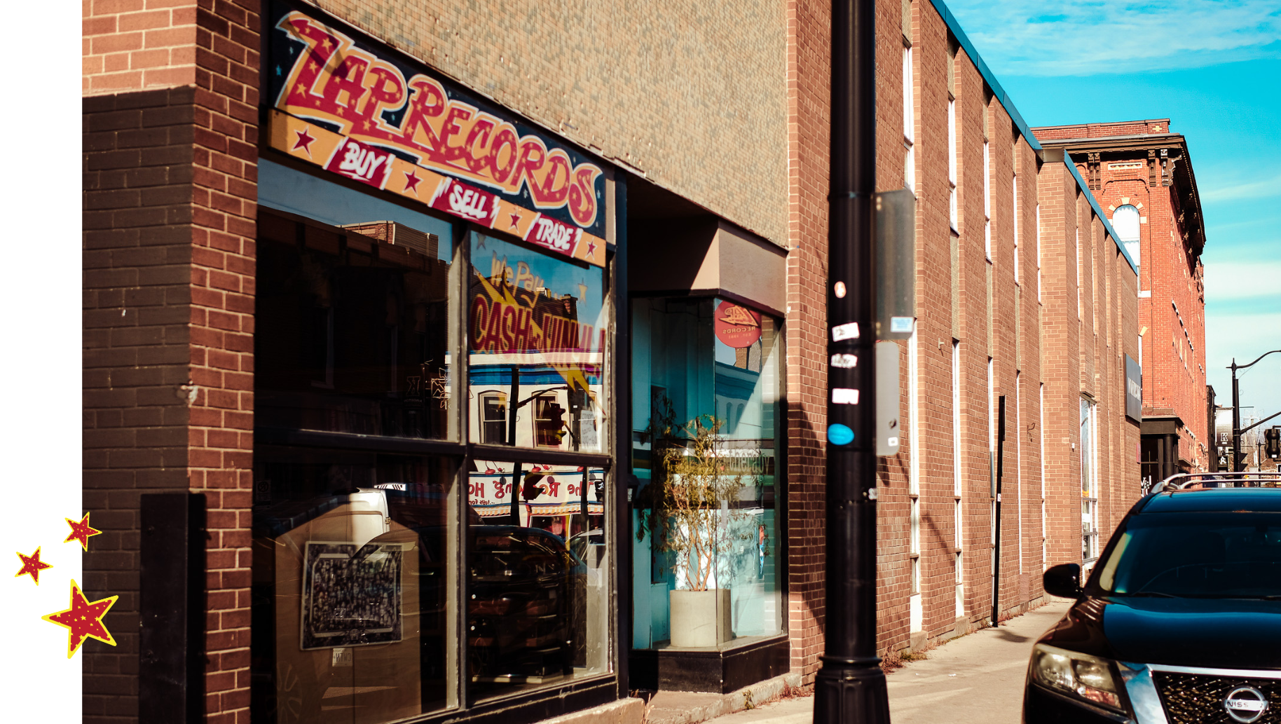 Street view of a brick building with a vintage record shop sign reading 'TARRECORDS' and a large window reflecting other storefronts and cars, with parked cars on the street and a clear blue sky.