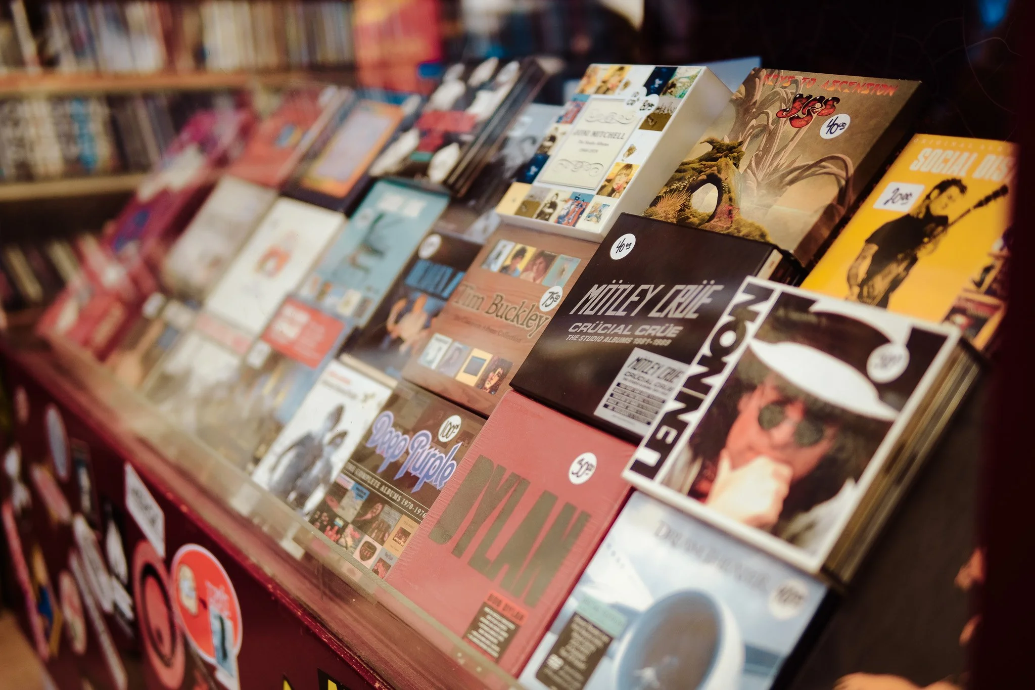 Display of vinyl records on a store shelf, including albums by Mötley Crüe, Kim Buckley, and other artists, with images of album covers and price tags visible.