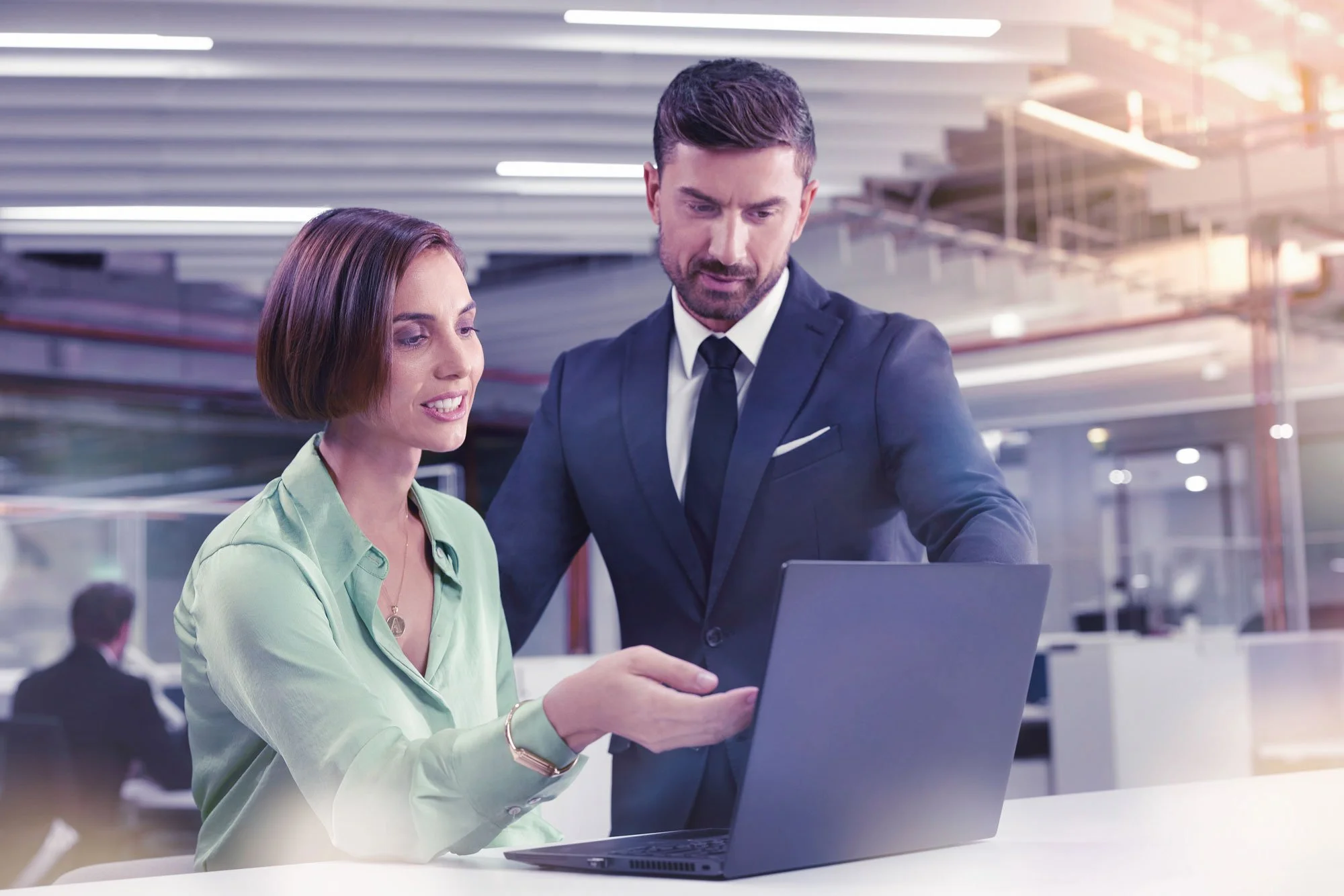 A woman and a man in business attire looking at a laptop in an office or conference room.
